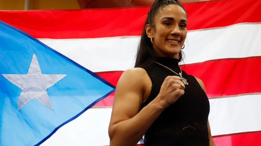 Amanda Serrano levantando sus cinturones mundiales de boxeo en el ring durante una pelea de peso pluma