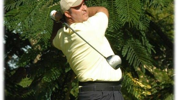 Golfista ejecuta un swing en un campo rodeado de árboles.
