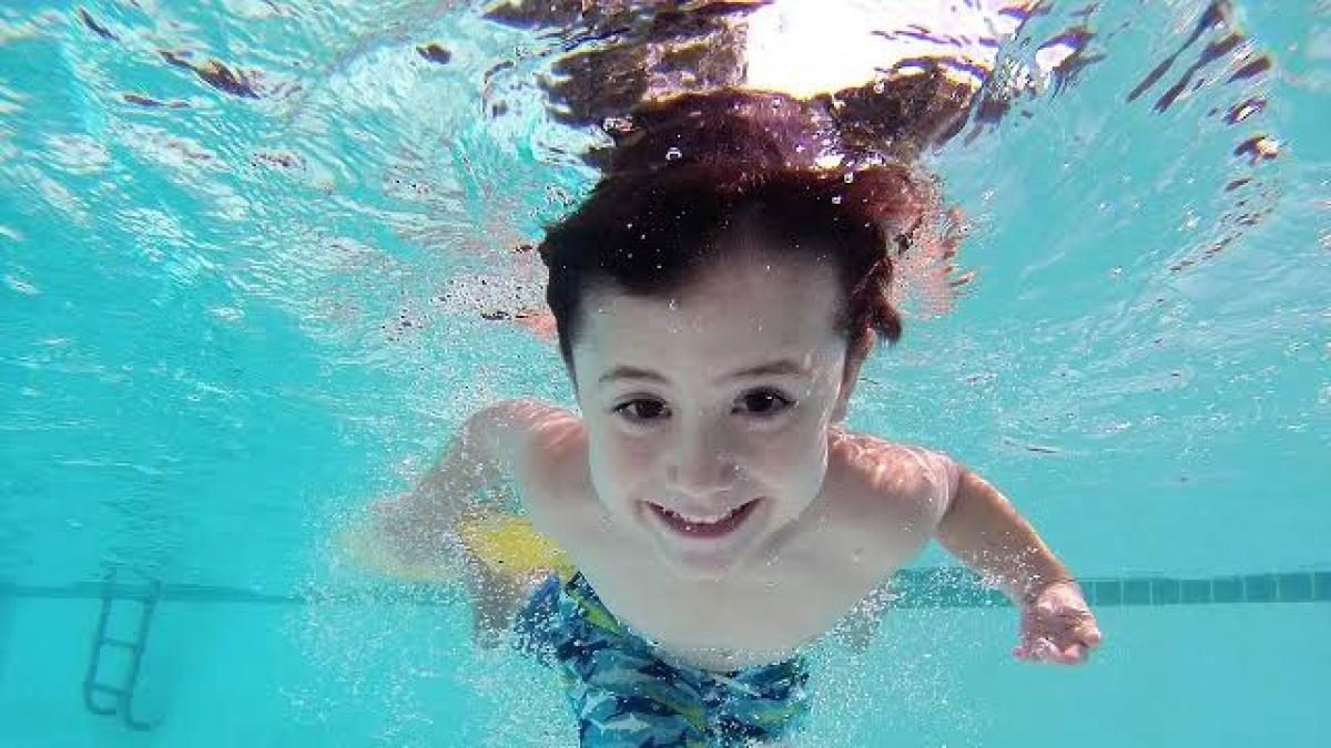 Niño con autismo entrando a una piscina acompañado por un instructor de natación adaptada