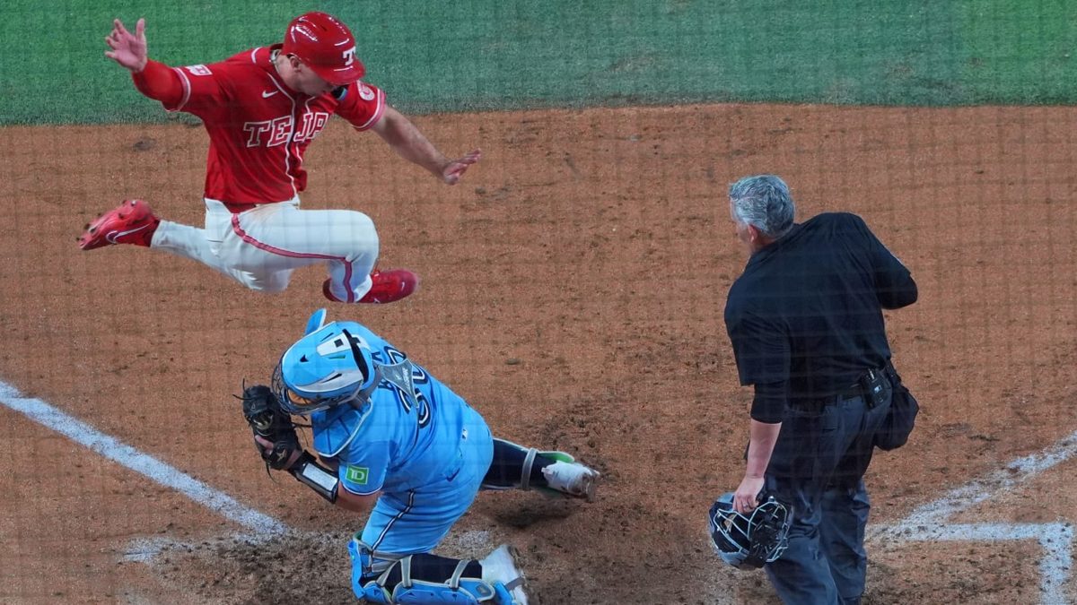 Wyatt Langford saltando sobre el catcher Alejandro Kirk en el plato durante el juego Rangers vs Blue Jays en Globe Life Field